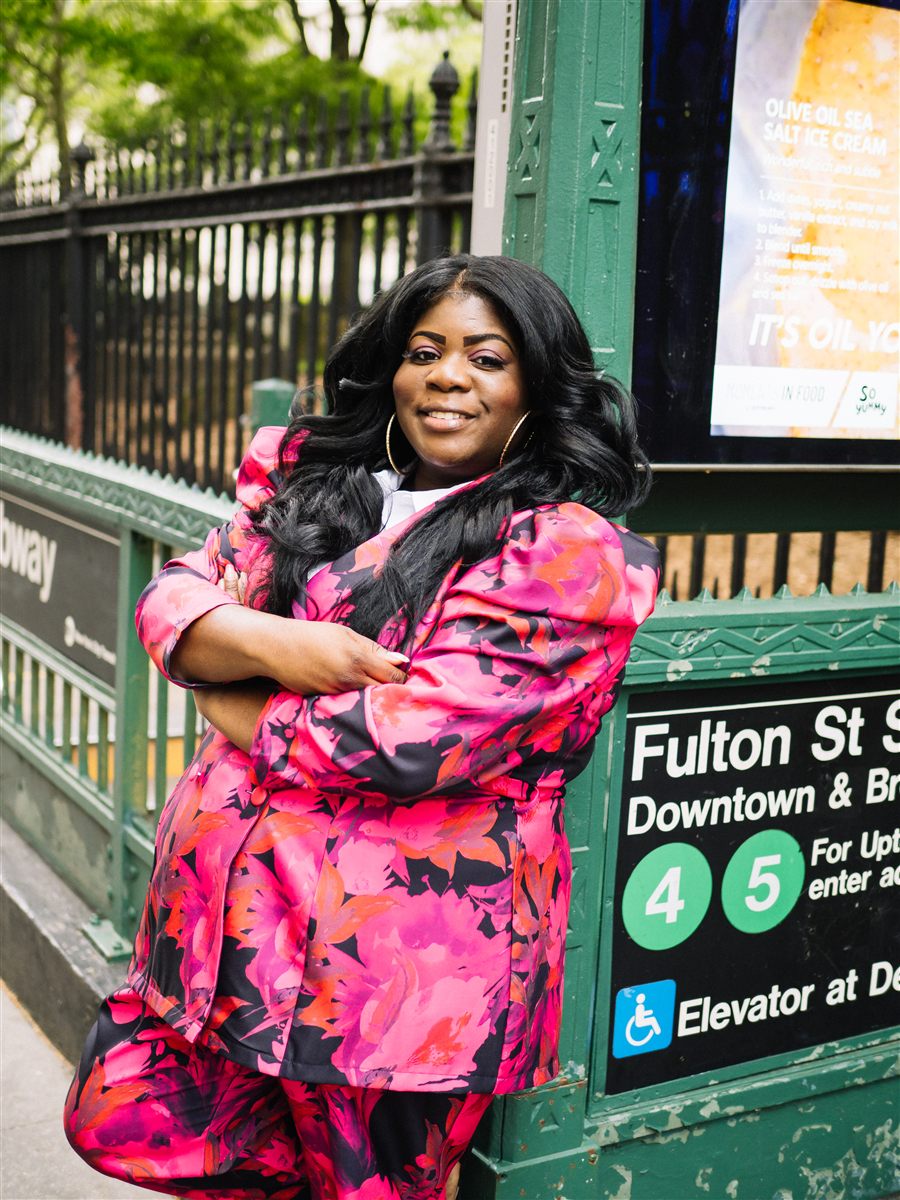 Danna Dennis smiling outside the Fulton St subway station in New York City.